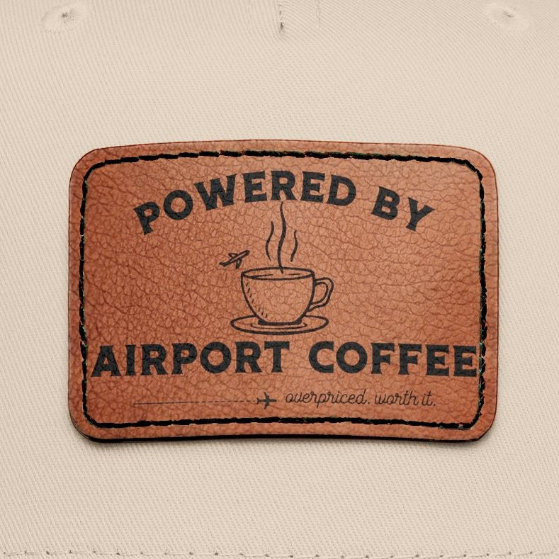 Beige and black cap with a brown leather patch displaying ''Powered by Airport Coffee" 
