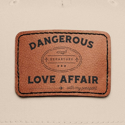 Beige and black cap with a brown leather patch displaying 'Dangerous Love Affair (with my passport)'