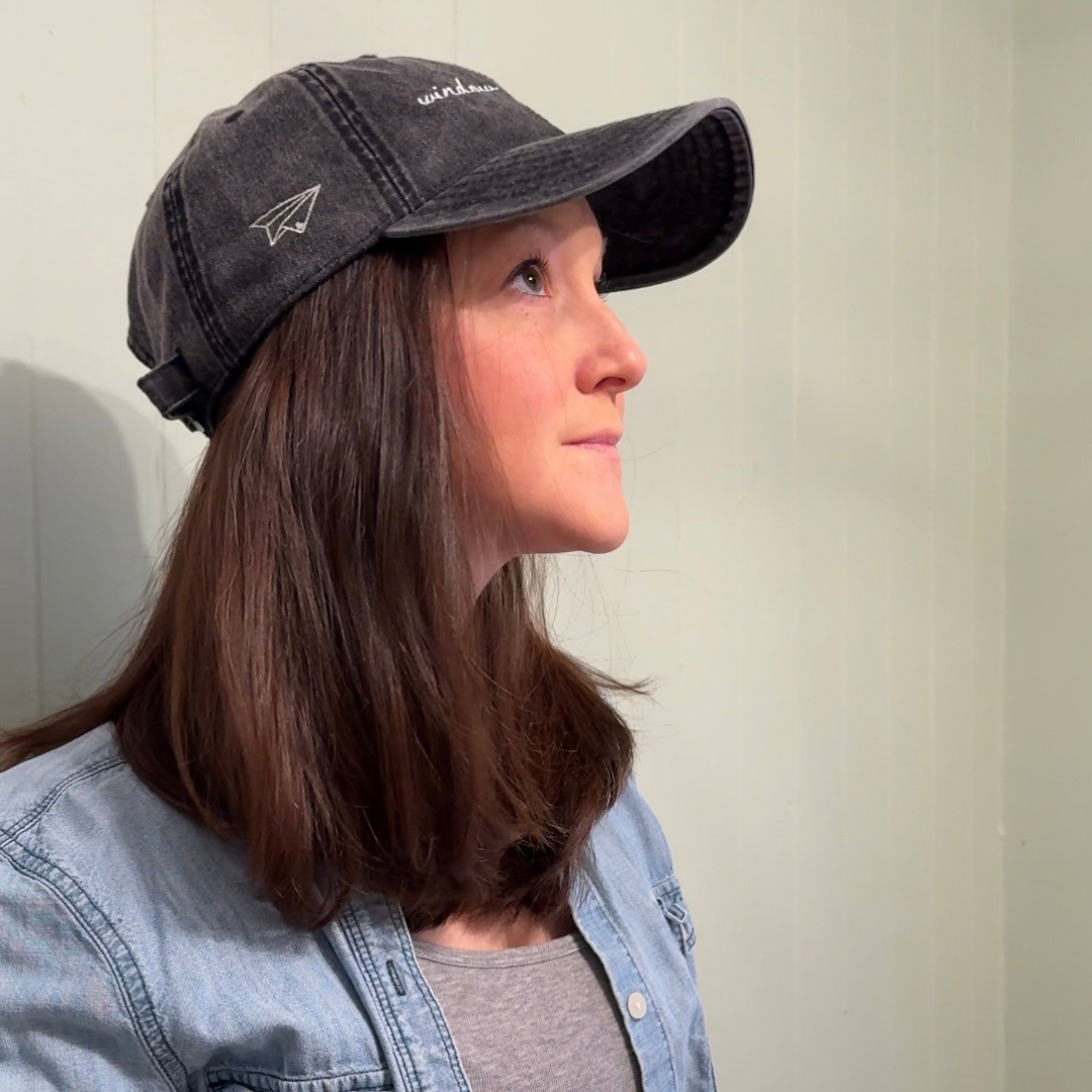 Person wearing a black cap with a logo and "window seat energy" against a plain background