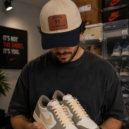 A man wearing a beige and navy cap with a brown patch featuring "Certified TSA regular (shoes off already)"