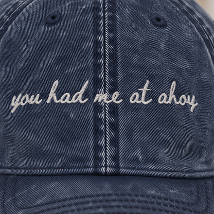 A close-up of a dark blue acid-wash cotton baseball cap with white embroidered text reading 'you had me at ohoy' on the front panel.