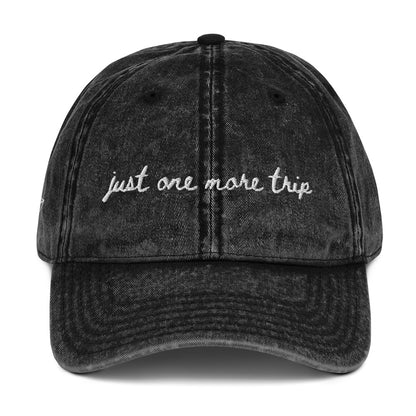 Vintage wash black travel themed hat with words "just one more trip" on it